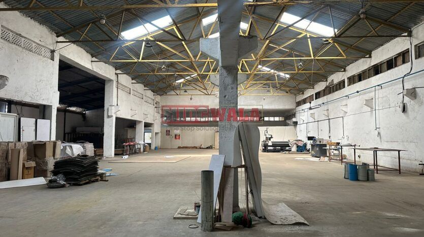 A well-lit industrial shed in the Taloja MIDC with large roller shutter doors and a spacious interior.
